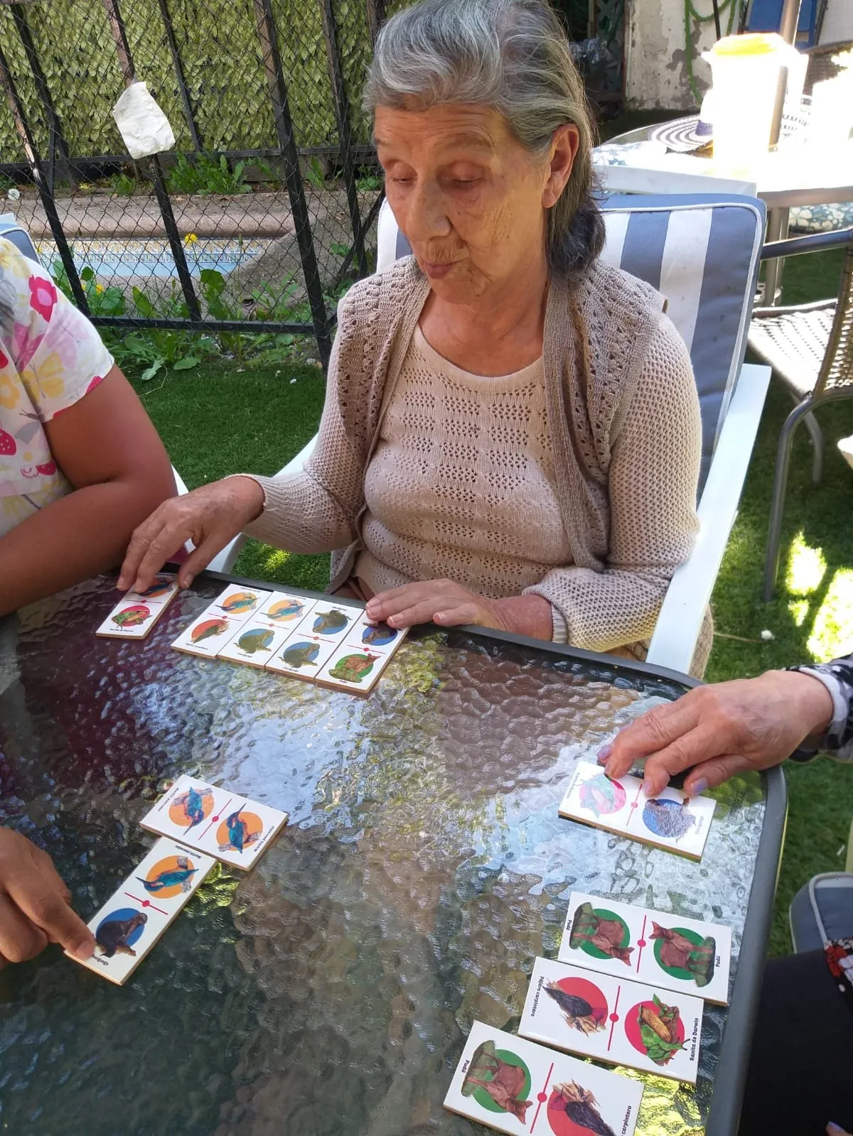 Una residente juega a las cartas en el jardín acompañada por una cuidadora